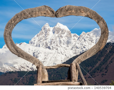 A large, rustic wooden heart frame and snow-capped peaks of Mount Ushba 140539704