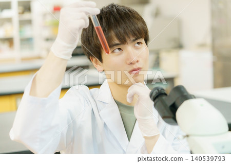 一位身穿白色實驗服的日本青年正在使用顯微鏡進行實驗、研究、開發和學習。 一位身穿白色實驗服的日本青年正在使用顯微鏡進行實驗、研究、開發和學習。 140539793
