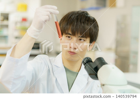 一位身穿白色實驗服的日本青年正在使用顯微鏡進行實驗、研究、開發和學習。 一位身穿白色實驗服的日本青年正在使用顯微鏡進行實驗、研究、開發和學習。 140539794