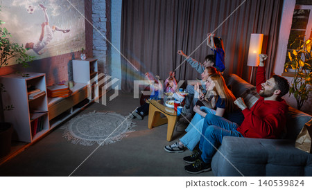 Happy family watching soccer projection at home during football fan night. Happy family watching soccer projection at home during football fan night. 140539824