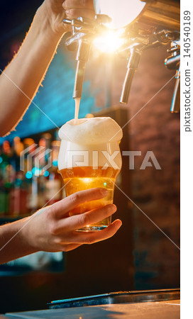 Female bartender pouring draft beer into glass with golden foam at bar Female bartender pouring draft beer into glass with golden foam at bar 140540189