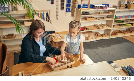 Early learning shelf area with girl exploring basket of smooth stones. 140540246