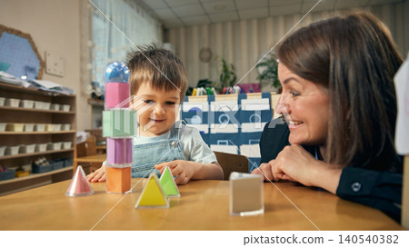 Joyful preschool activity with toddler building tower from colorful geometric shapes. 140540382