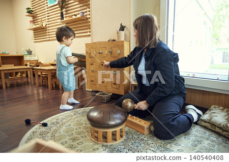 Toddler exploring wooden activity board while educator guides fine motor learning 140540408