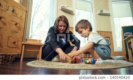 Teacher helping toddler play with wooden toys in preschool classroom close up. 140540420