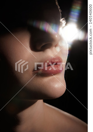 Macro beauty close up of glossy lips and skin with lens flare in dark studio light. 140540600
