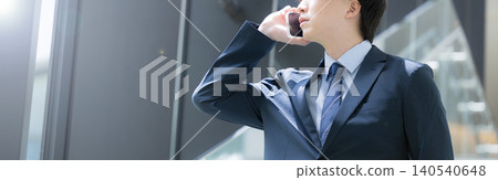A handsome, middle-aged businessman walking up and down the stairs in the office while talking on his smartphone – a typical sales image. A handsome, middle-aged businessman walking up and down the stairs in the office while talking on his smartphone – a typical sales image. 140540648