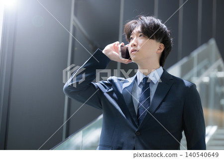 A handsome, middle-aged businessman walking up and down the stairs in the office while talking on his smartphone – a typical sales image. A handsome, middle-aged businessman walking up and down the stairs in the office while talking on his smartphone – a typical sales image. 140540649