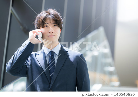 A handsome, middle-aged businessman walking up and down the stairs in the office while talking on his smartphone – a typical sales image. A handsome, middle-aged businessman walking up and down the stairs in the office while talking on his smartphone – a typical sales image. 140540650