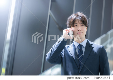 一位英俊的中年商人一邊用智慧型手機通話,一邊在辦公室的樓梯上走來走去——典型的銷售形象。 一位英俊的中年商人一邊用智慧型手機通話,一邊在辦公室的樓梯上走來走去——典型的銷售形象。 140540651