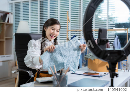 Asia vlogger woman influencer, SME retail store owner smile enjoy selling clothes live online screen smartphone and laptop work at home. 140541002