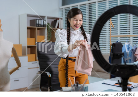 Asia vlogger woman influencer, SME retail store owner smile enjoy selling clothes live online screen smartphone and laptop work at home. Asia vlogger woman influencer, SME retail store owner smile enjoy selling clothes live online screen smartphone and laptop work at home. 140541008