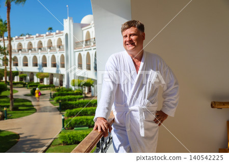 Russian male tourist enjoying bright warm sunshine on a hotel balcony during a relaxing vacation getaway Russian male tourist enjoying bright warm sunshine on a hotel balcony during a relaxing vacation getaway 140542225