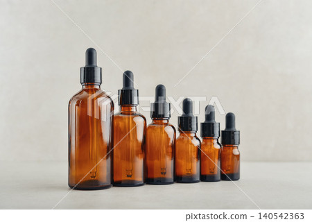 Amber glass dropper bottles of different sizes arranged in ascending order from smallest to largest on light background. Amber glass dropper bottles of different sizes arranged in ascending order from smallest to largest on light background. 140542363
