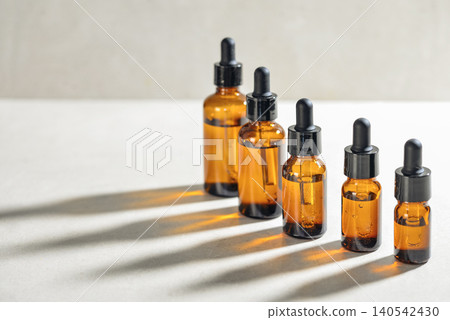 Amber glass dropper bottles of different sizes arranged in ascending order from smallest to largest on light background. Amber glass dropper bottles of different sizes arranged in ascending order from smallest to largest on light background. 140542430