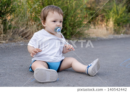 Cute little toddler sitting on an asphalt path outdoors in summer Cute little toddler sitting on an asphalt path outdoors in summer 140542442