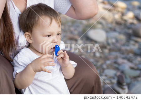 Close-up portrait of a toddler with a pacifier held by mother outdoors 140542472