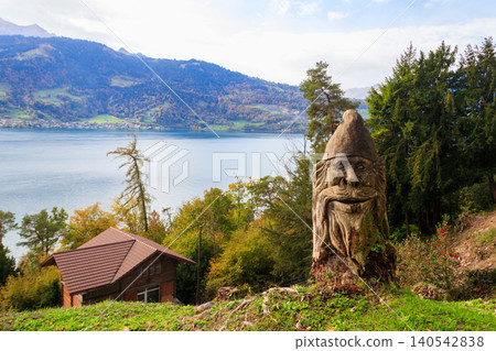 Autumn view of the Lake Thun from St. Beatus Caves entrance in Beatenberg, Bernese Oberland, Switzerland. Carved wooden statue in a foreground Autumn view of the Lake Thun from St. Beatus Caves entrance in Beatenberg, Bernese Oberland, Switzerland. Carved wooden statue in a foreground 140542838