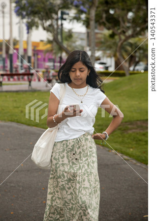 A young girl is walking down a sidewalk while looking at her cell phone 140543371