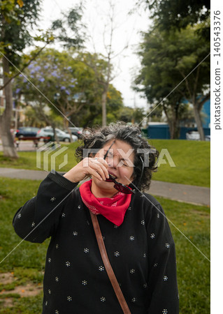 A woman is drinking a beverage while wearing a red bandana A woman is drinking a beverage while wearing a red bandana 140543376