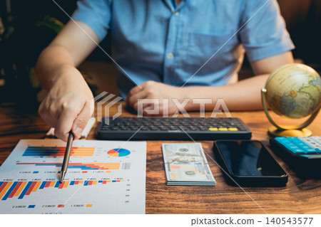 Business professional analyzing financial charts and graphs with cash, smartphone, and calculator on wooden desk 140543577