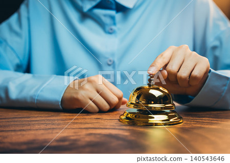Elegant Gold Service Bell on Wooden Counter, Customer Interacting with Receptionist in Hospitality Setting Elegant Gold Service Bell on Wooden Counter, Customer Interacting with Receptionist in Hospitality Setting 140543646