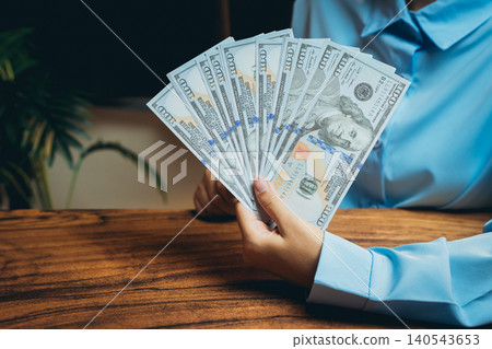 Elegant Hand Holding Fanned Stack of Money on Wooden Table in Professional Setting 140543653
