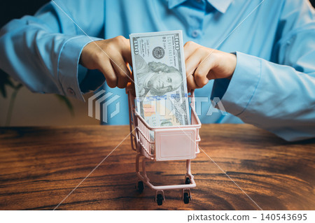 Hands Placing Dollar Bills into Small Shopping Cart Representing Money Management and Financial Transactions 140543695
