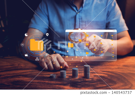 File management concept. Digital data analysis with a magnifying glass over file icons and stacked coins on a wooden table background File management concept. Digital data analysis with a magnifying glass over file icons and stacked coins on a wooden table background 140543737