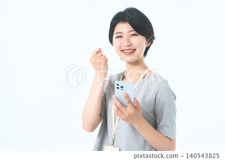 一位面帶微笑的年輕女子手持智慧型手機，輕輕揮動拳頭。 140543825