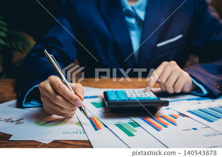 Business professional analyzing financial graphs while using calculator during office meeting for strategic planning Business professional analyzing financial graphs while using calculator during office meeting for strategic planning 140543878