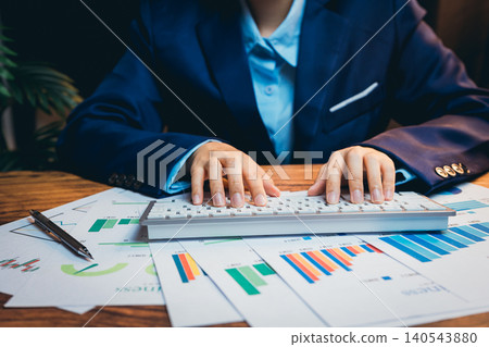Professional Business Person Analyzing Financial Data with Keyboard Surrounded by Charts and Graphs on Desk Professional Business Person Analyzing Financial Data with Keyboard Surrounded by Charts and Graphs on Desk 140543880