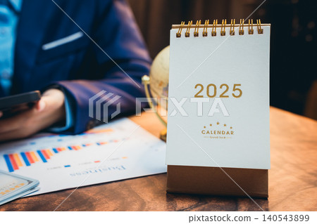 Desk Calendar for Year 2025 with Business Charts and Globe in Office Environment Desk Calendar for Year 2025 with Business Charts and Globe in Office Environment 140543899