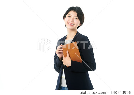 A young woman in a jacket smiles while holding a binder. A young woman in a jacket smiles while holding a binder. 140543906
