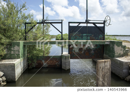 A water control gate system manages water flow in an agricultural canal used for rice farming. This system supports sustainable practices in a protected wetland area. A water control gate system manages water flow in an agricultural canal used for rice farming. This system supports sustainable practices in a protected wetland area. 140543966