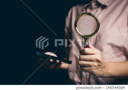 Person Holding Magnifying Glass and Mobile Phone Against Dark Background for Analysis and Investigation Theme Person Holding Magnifying Glass and Mobile Phone Against Dark Background for Analysis and Investigation Theme 140544084