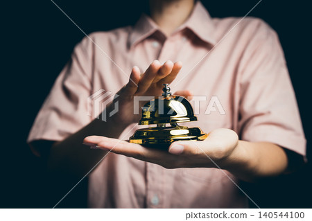 Elegant Gold Service Bell with Hand on Dark Background for Hospitality and Reception Themes Elegant Gold Service Bell with Hand on Dark Background for Hospitality and Reception Themes 140544100