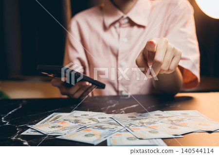Person Holding Phone and Pointing at Cash on Table in Modern Interior Setting Person Holding Phone and Pointing at Cash on Table in Modern Interior Setting 140544114