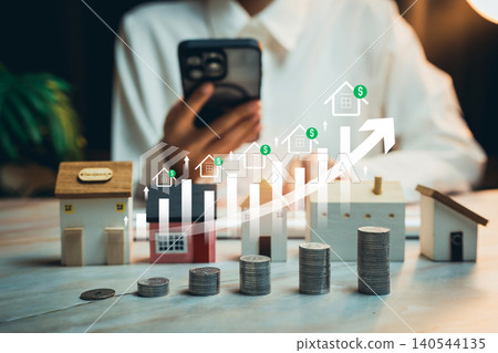 Real estate investment growth concept. Person using smartphone behind miniature houses and stacked coins with rising property value chart, housing market investment strategy Real estate investment growth concept. Person using smartphone behind miniature houses and stacked coins with rising property value chart, housing market investment strategy 140544135