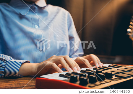 Pianist concept. Person Playing a MIDI Keyboard in a Home Studio Setting with Soft Lighting and Modern Decor 140544190