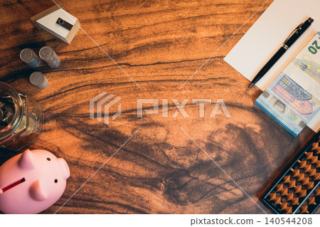 Business concept. Workspace with financial tools, piggy bank, cash notes, paper, pen, and coins arranged on wooden desk surface Business concept. Workspace with financial tools, piggy bank, cash notes, paper, pen, and coins arranged on wooden desk surface 140544208
