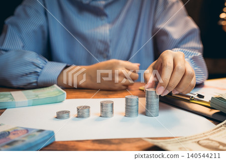 Business concept. Person Counting Stacked Coins on Table Surrounded by Banknotes and Financial Documents in Office Setting Business concept. Person Counting Stacked Coins on Table Surrounded by Banknotes and Financial Documents in Office Setting 140544211