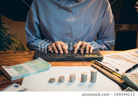 Business concept. Focused Person Working on Financial Analysis with Cash and Charts on Desk at Home Office Setting Business concept. Focused Person Working on Financial Analysis with Cash and Charts on Desk at Home Office Setting 140544213