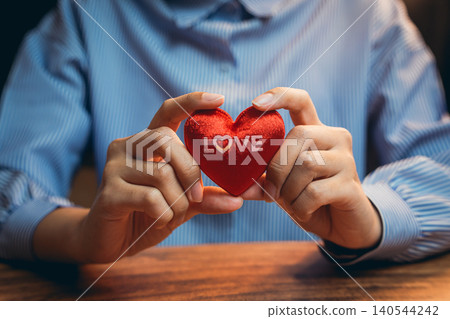 Love concept. Person Holding Red Heart Shaped Decoration with Love Text on Table for Romantic Themes and Celebrations 140544242