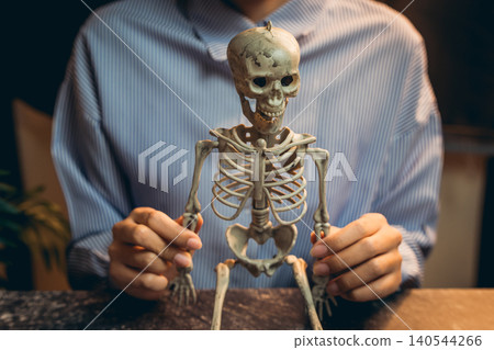 Halloween prop concept. Human Skeleton Model Held by a Person in Striped Shirt for Educational and Artistic Purposes Halloween prop concept. Human Skeleton Model Held by a Person in Striped Shirt for Educational and Artistic Purposes 140544266