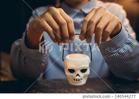 Halloween prop concept. Person Holding a Skull-Shaped Candle Holder with a Dark Background for Halloween or Spooky Theme Halloween prop concept. Person Holding a Skull-Shaped Candle Holder with a Dark Background for Halloween or Spooky Theme 140544277
