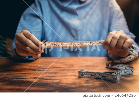 Close-up of Hands Measuring with Tape Measure on Wooden Table in Cozy Indoor Setting Close-up of Hands Measuring with Tape Measure on Wooden Table in Cozy Indoor Setting 140544280