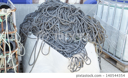Thick grey mooring ropes are stored in a white plastic container at a commercial port. This location supports the fishing and maritime industries in daily operations. Thick grey mooring ropes are stored in a white plastic container at a commercial port. This location supports the fishing and maritime industries in daily operations. 140544354