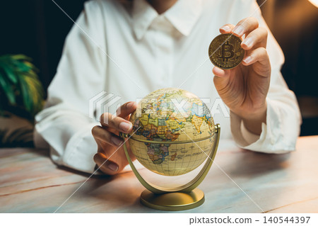 Money concept. Business Person Holding Bitcoin while Looking at Globe in Modern Office Setting with Focus on Cryptocurrency and Travel Money concept. Business Person Holding Bitcoin while Looking at Globe in Modern Office Setting with Focus on Cryptocurrency and Travel 140544397