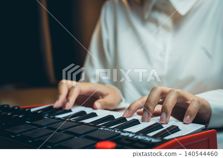 Pianist Concept. Close-Up of Hands Playing a Small Keyboard Synthesizer in a Softly Lit Environment Pianist Concept. Close-Up of Hands Playing a Small Keyboard Synthesizer in a Softly Lit Environment 140544460
